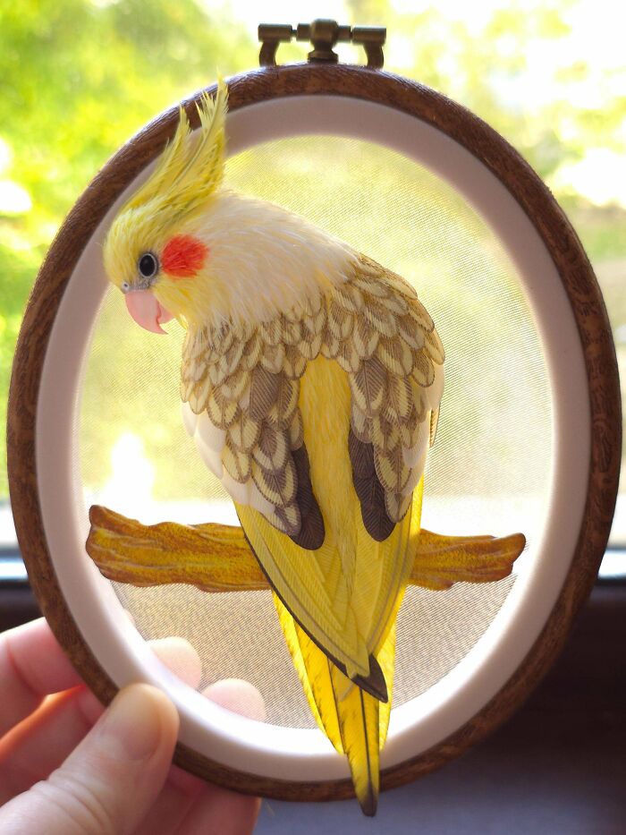An exquisite handmade project: a detailed yellow cockatiel embroidered in a hoop, sitting on a branch.