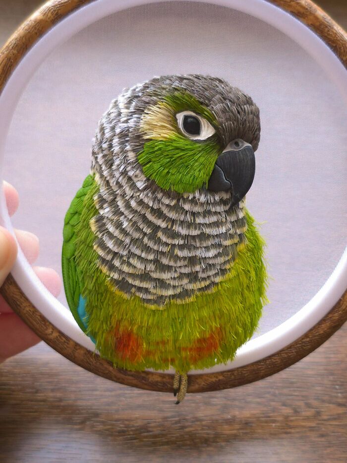 A detailed handmade project of a green parrot embroidered within a circular hoop, showcasing intricate feather work.