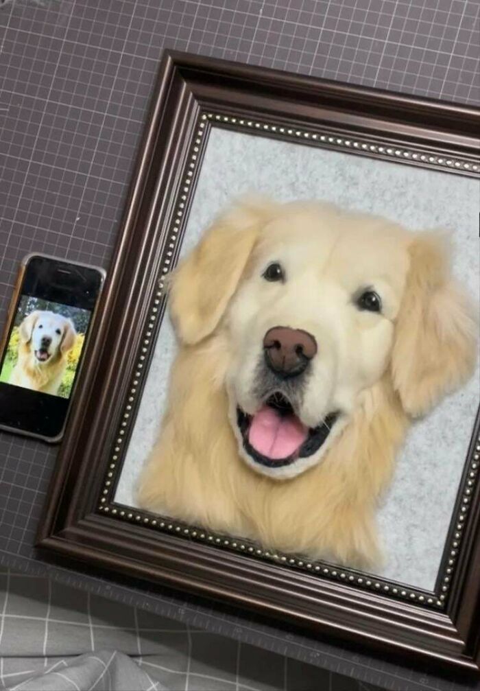 A framed handmade project of a realistic golden retriever face made from felt next to a phone displaying the dog's photo.