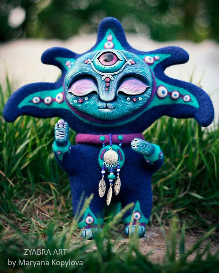 A handmade project of a blue and green plush alien-like creature with an eye on its forehead, standing in grass.