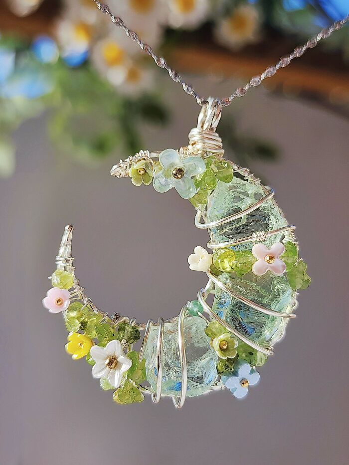 A crescent moon-shaped pendant crafted from wire-wrapped glass and small flowers, a beautiful handmade project.