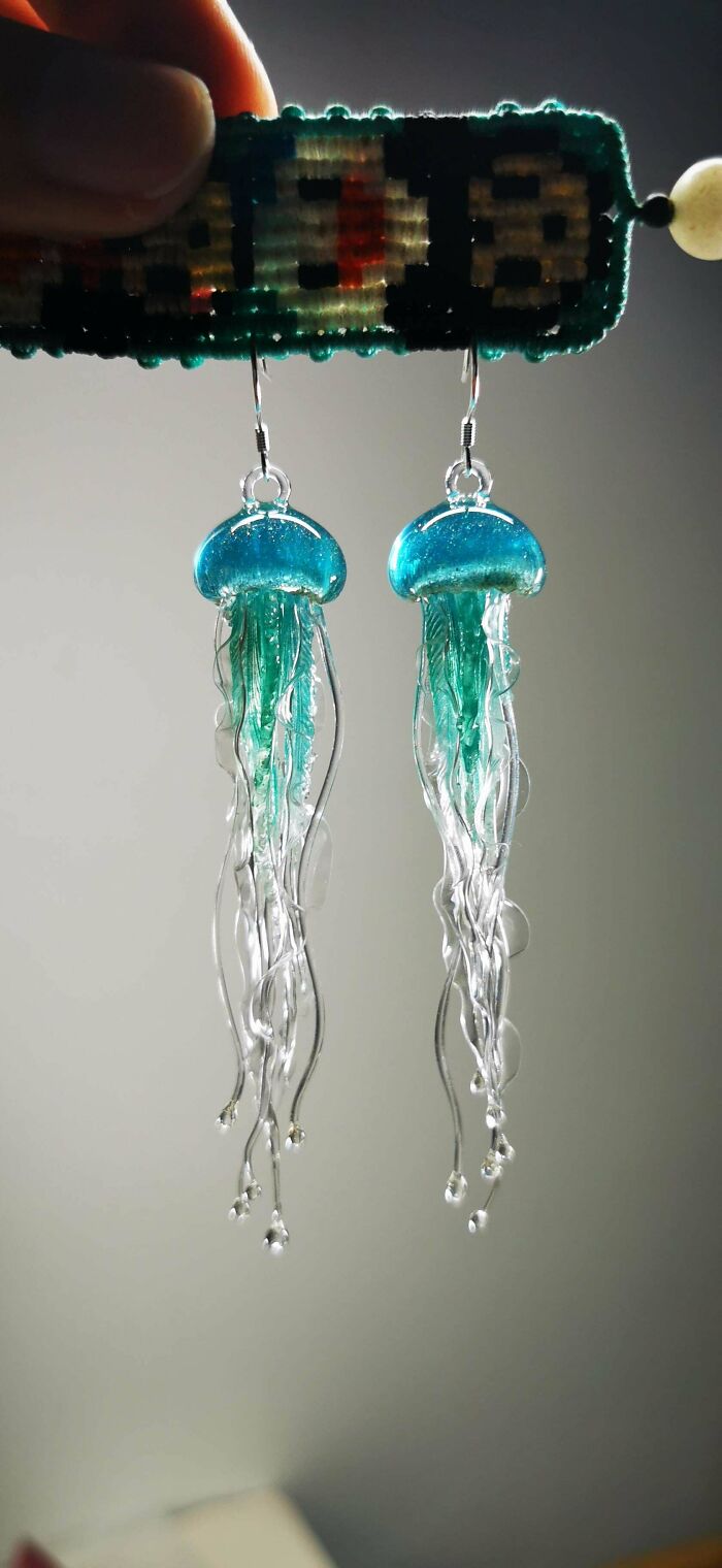 Two delicate blue and clear jellyfish-shaped handmade earrings dangling, highlighting intricate handmade projects.