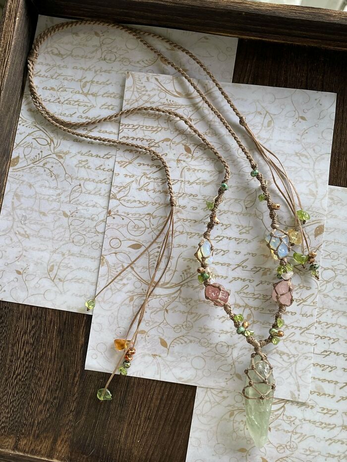 A delicate handmade project of a macrame necklace adorned with various gemstone beads and a large clear crystal pendant.