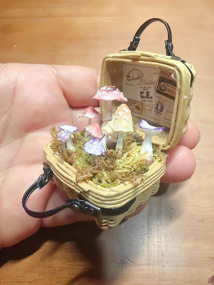A tiny, open handmade basket project containing miniature mushrooms and moss, held in a person's hand.