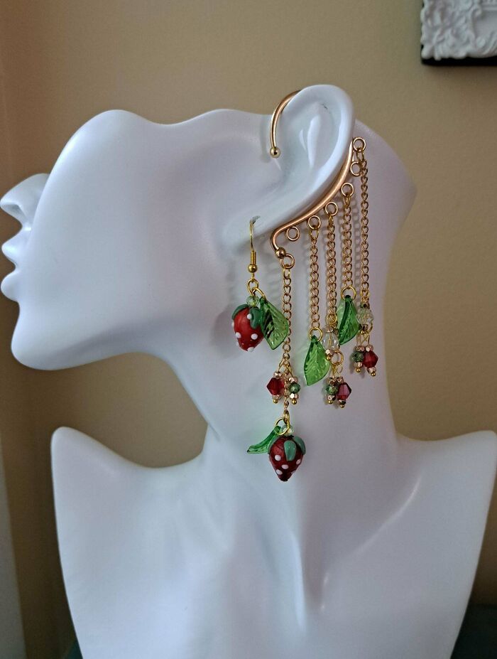 A unique handmade project of an elaborate ear cuff with strawberry charms and green leaves on a white mannequin.