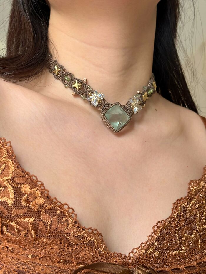 A woman wearing a handmade macrame necklace with a large green gemstone and floral beadwork. A beautiful handmade project.