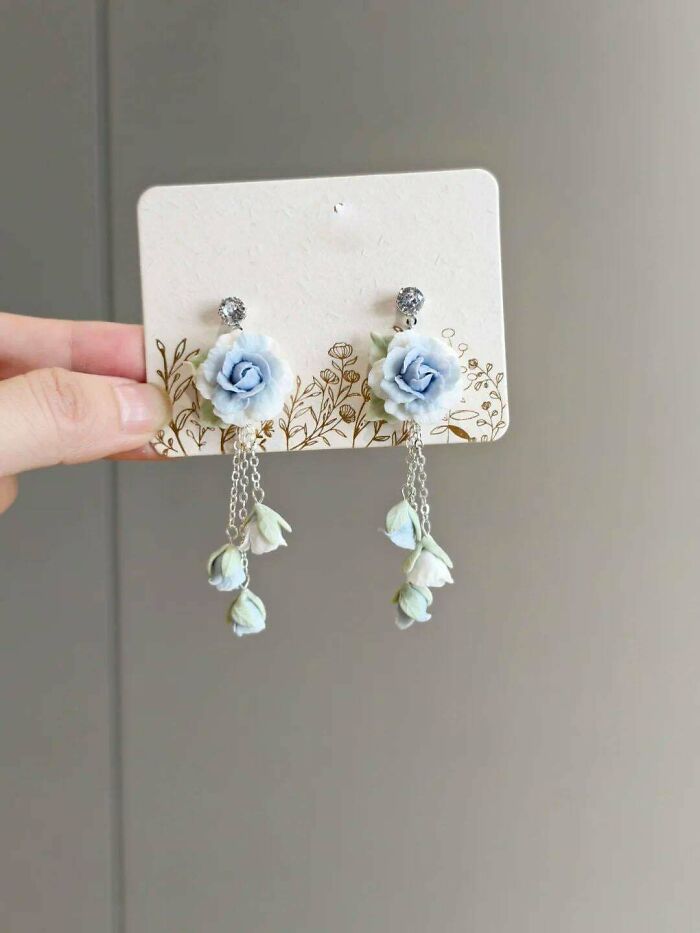 A pair of delicate handmade projects: dangling earrings with blue flowers and small buds.
