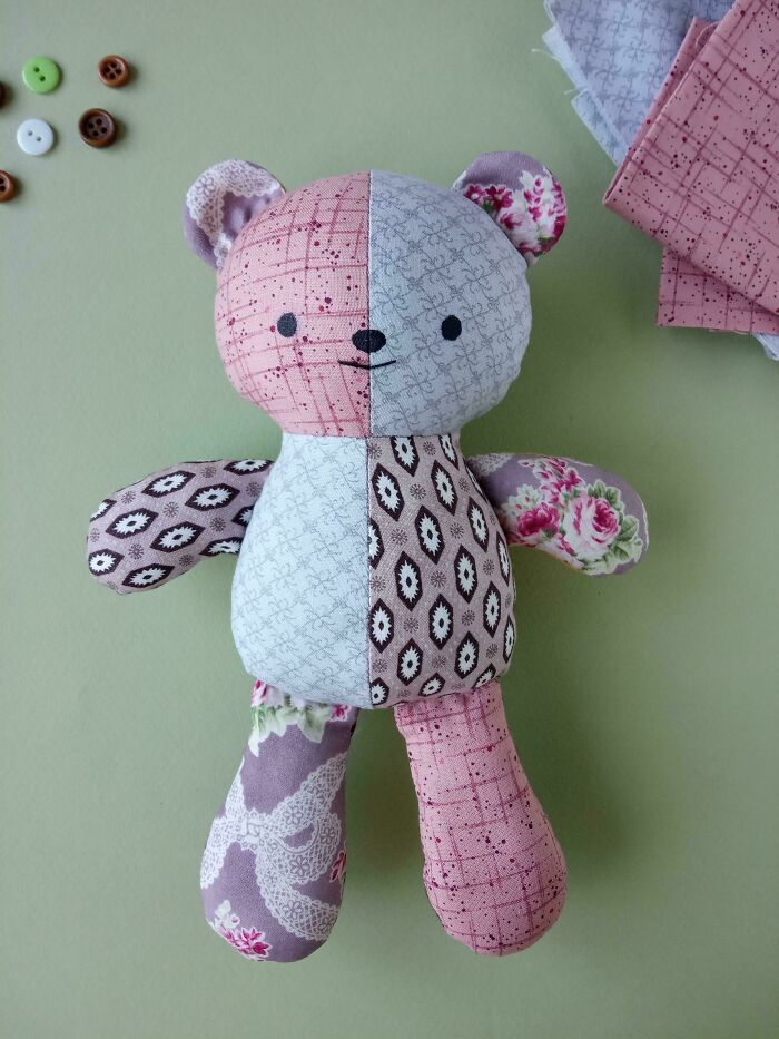 A charming, patchwork teddy bear, a delightful handmade project, lying on a soft green background with buttons.