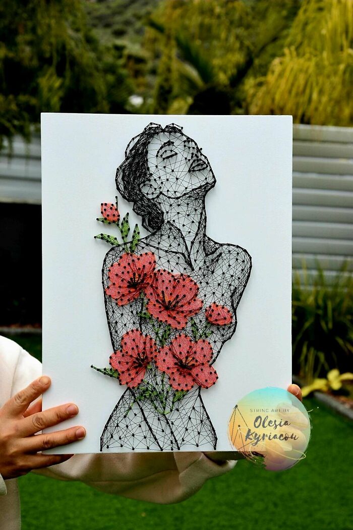 A person holding a stunning string art handmade project depicting a woman with flowing floral patterns.