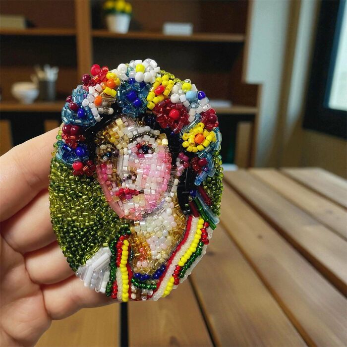A close-up of a vibrant, handmade projects brooch featuring a woman's face adorned with colorful beads.
