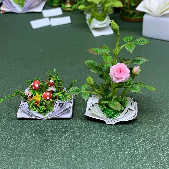 Miniature handmade projects of a pink rose and red mushrooms on open books, showcasing intricate details.