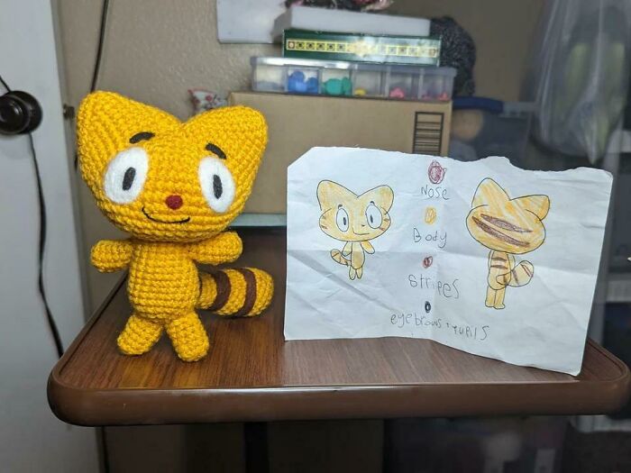 A handmade crocheted yellow cat doll next to a drawing of the character, illustrating creative handmade projects.