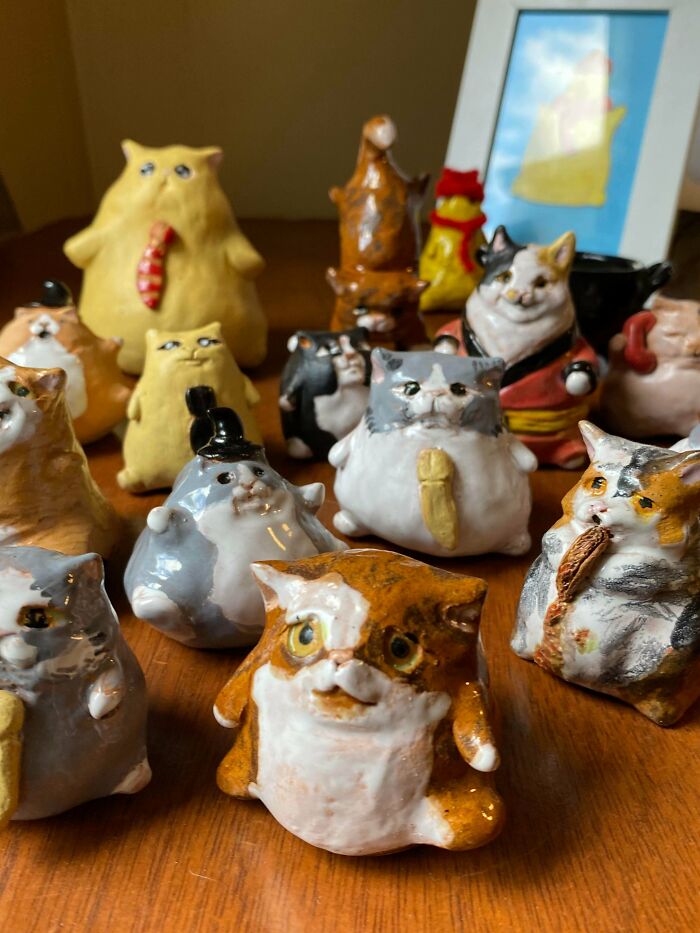Collection of various handmade ceramic cat figurines on a wooden table, showcasing diverse handmade projects.
