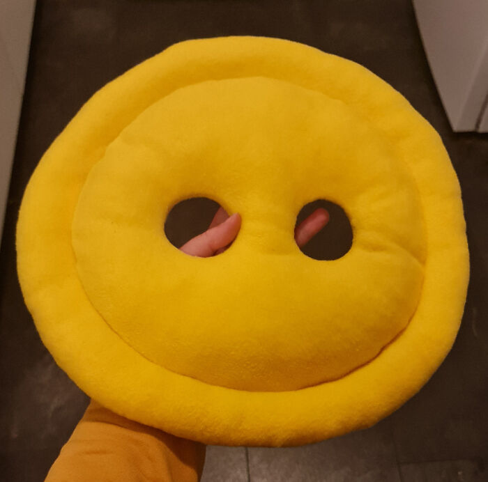 A handmade projects yellow smiley face button pillow with two dark buttonholes, held by a hand.