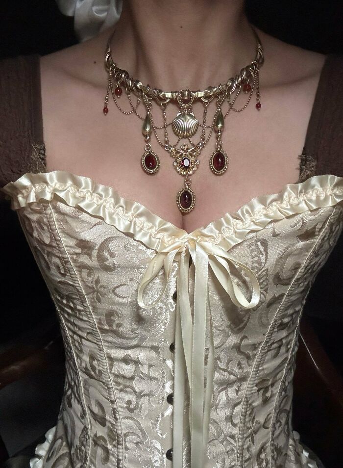 A person wearing an elaborate gold and red gemstone handmade necklace over a cream corset, highlighting handmade projects.