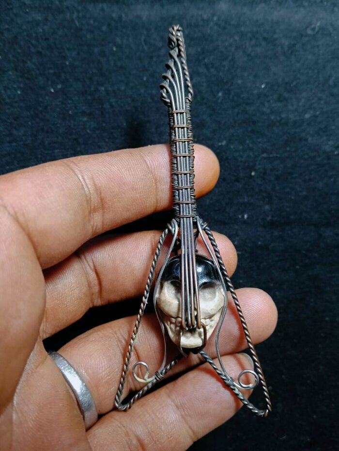 A handmade projects miniature guitar with a skull at its base, made from wire and bone, held by a hand.