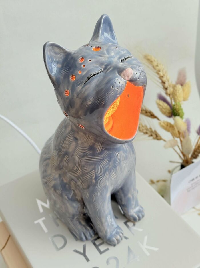 A charming handmade project of a gray ceramic cat lamp with an open mouth, glowing orange, highlighting artistic handmade projects.