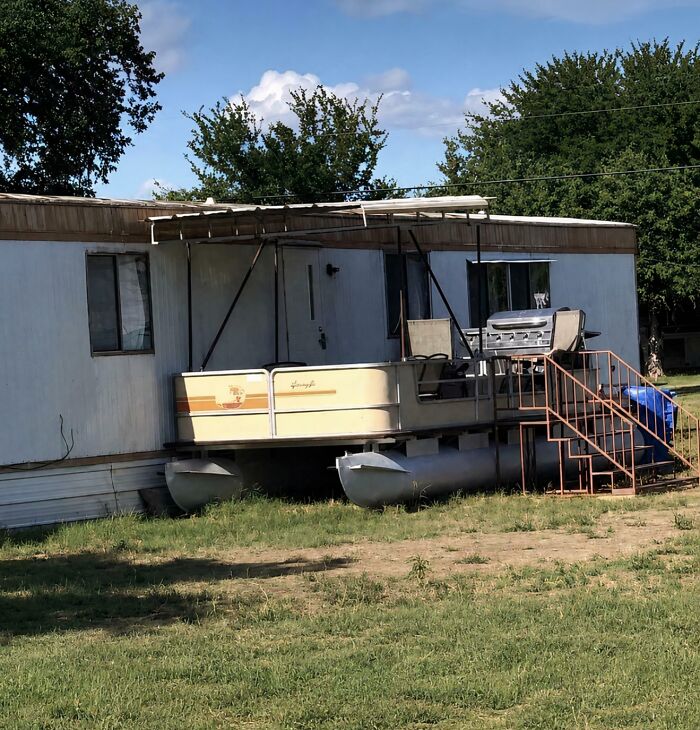 A pontoon boat serving as a porch for a mobile home, showcasing clever solutions from random junk.