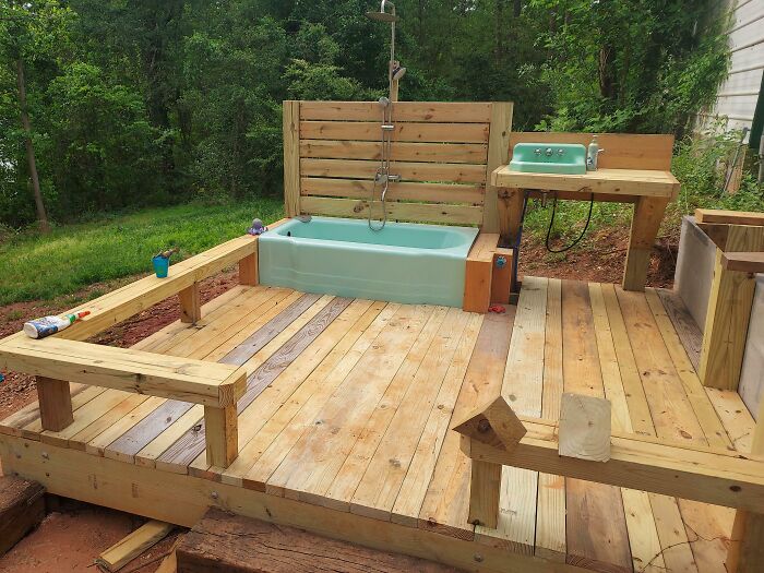 An outdoor wooden deck with a turquoise bathtub and sink, a clever solution for a unique exterior bathing area.