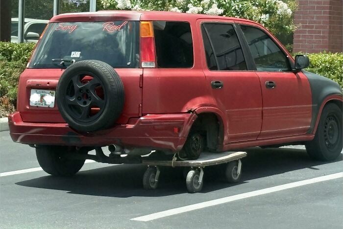A red SUV with one back wheel missing, replaced by a skateboard. This is a clever solution for random junk.
