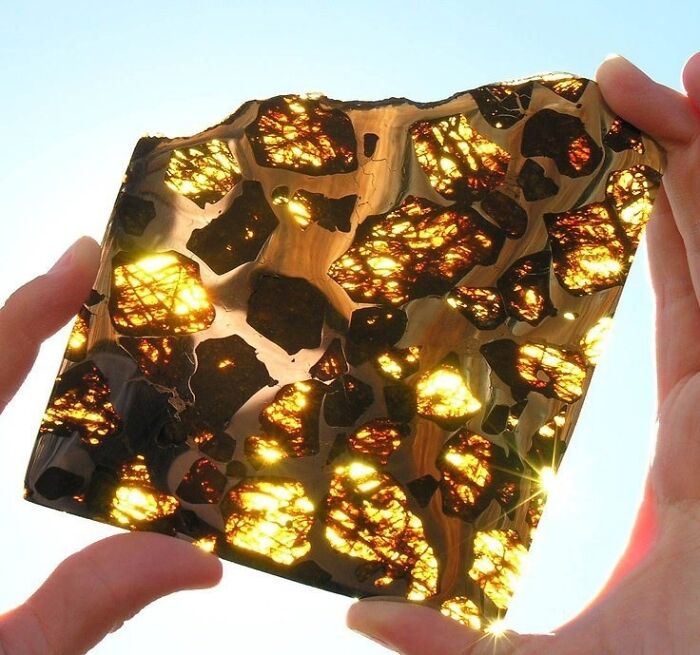 Interesting and surprising photo of a meteorite cut in half, revealing glowing crystals when held against light.