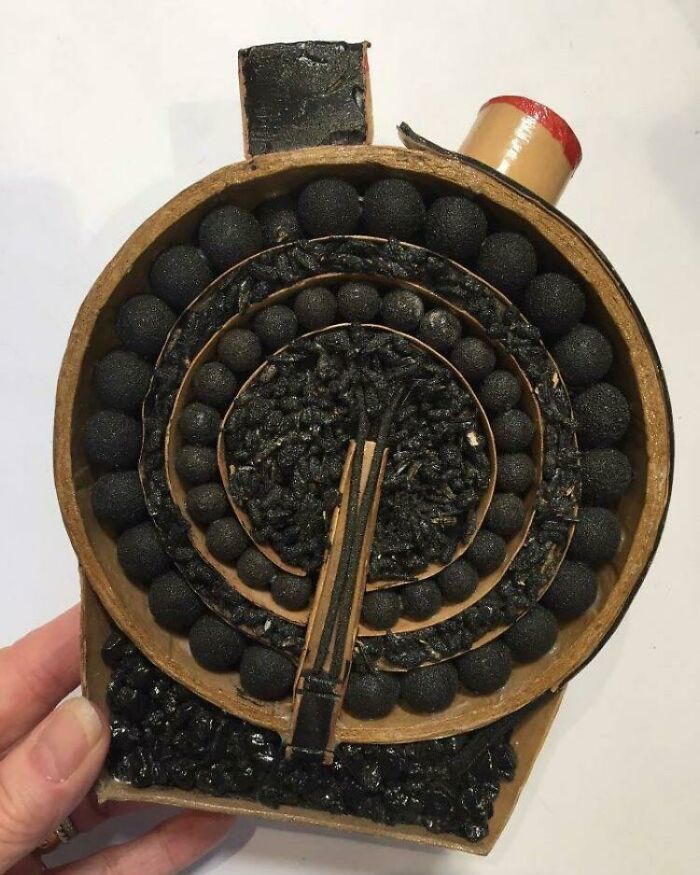 A hand holding an object cut in half, revealing a spiral of small black spheres and granular material inside.