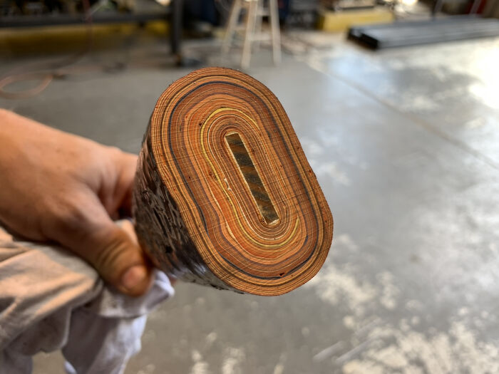A hand holding an object cut in half, showing many layers of different colored materials, resembling wood grain.