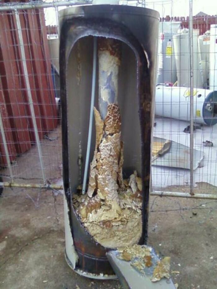 An old water heater tank cut in half, revealing a large buildup of sediment and corrosion inside the object.