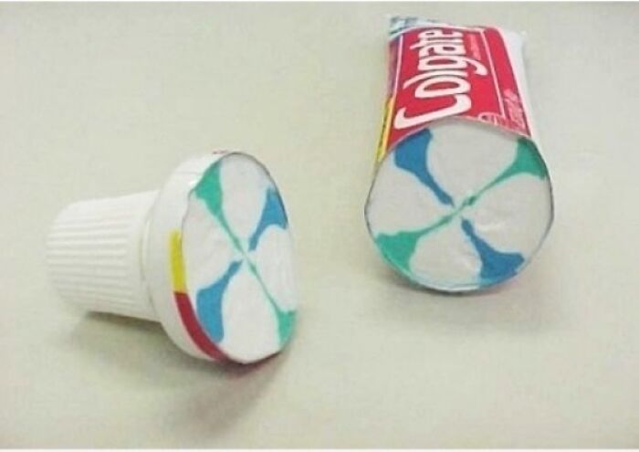 A Colgate toothpaste tube cut in half, showing the colorful striped paste inside, a surprising photo of an object cut in half.