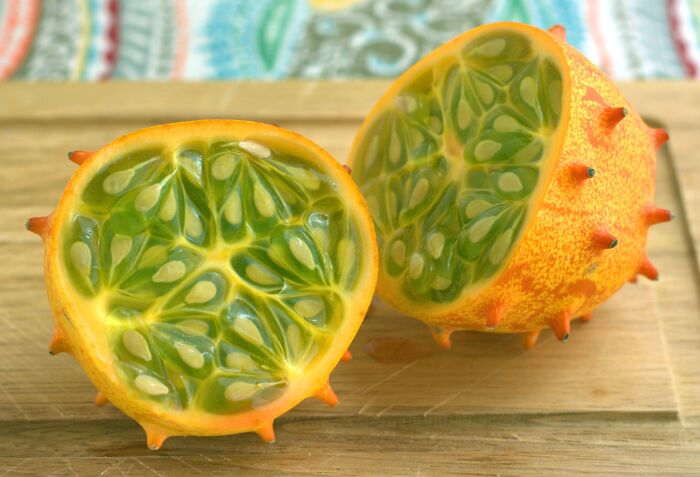 A vibrant horned melon (kiwano) cut in half, showing its bright green, gelatinous interior with numerous seeds.