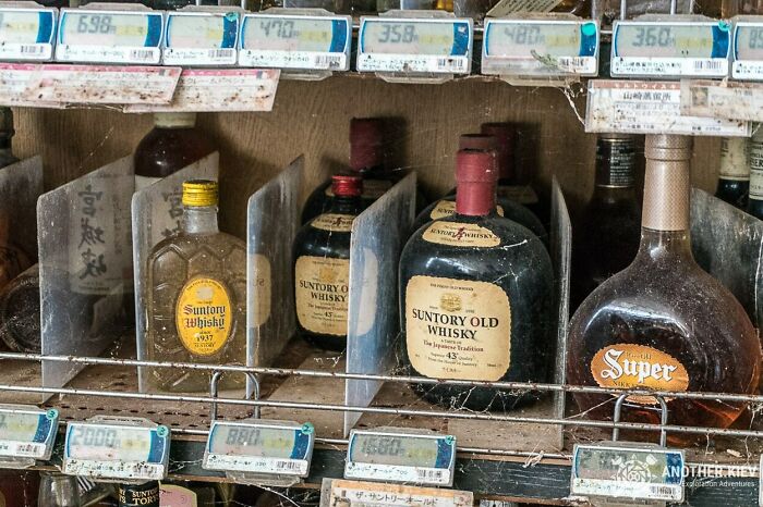 Dusty bottles of Suntory Old Whisky and Suntory Whisky, unexpected finds in exploring abandoned places, sit on a cobwebbed shelf.