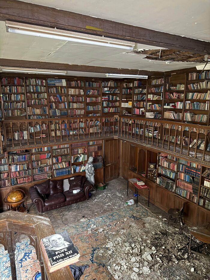 A grand, multi-level library in abandoned places with extensive bookshelves, a leather couch, and debris on the floor, revealing something very unexpected.