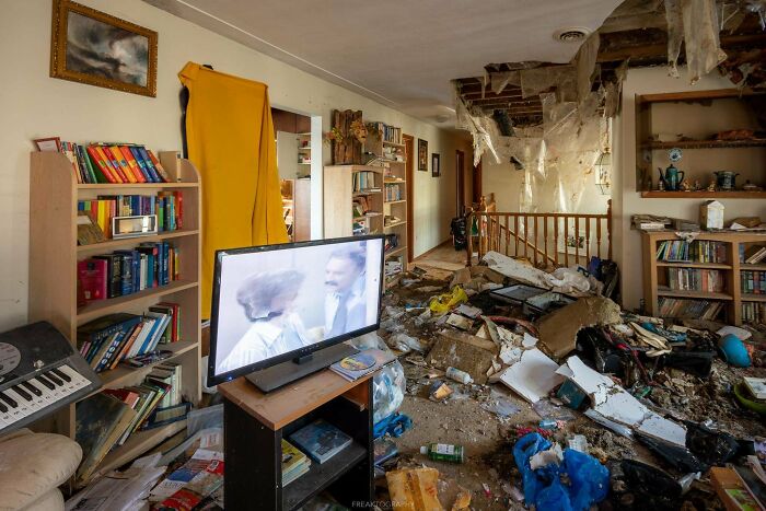 A living room in an abandoned place with a TV showing a show, surrounded by debris and collapsed ceiling, exploring unexpected finds.