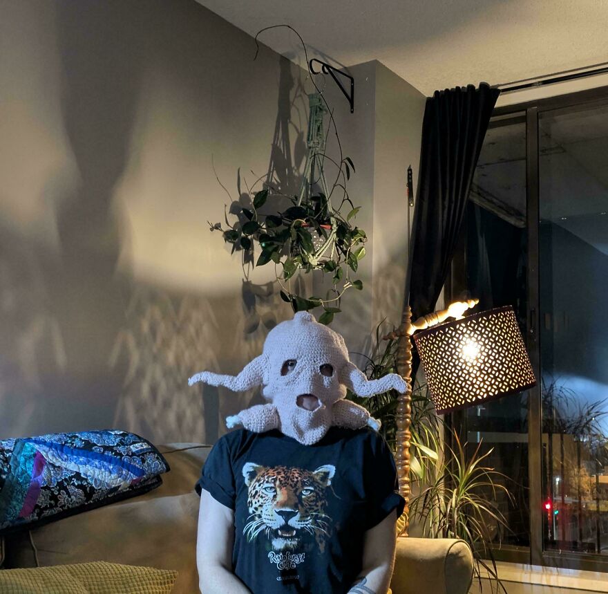 A person wearing a light pink, octopus-like crochet creation over their head indoors, showing not every craft project turns out as intended.