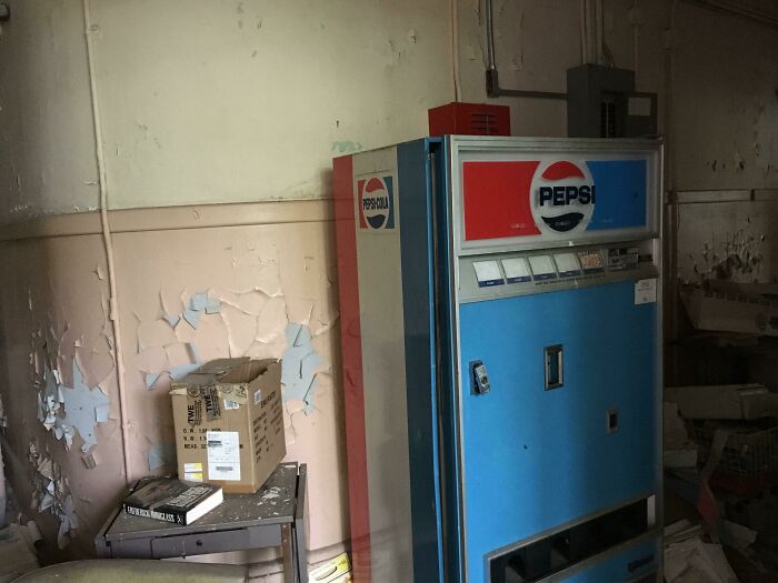 An old, dirty Pepsi vending machine in an abandoned room with peeling paint, exploring abandoned places.