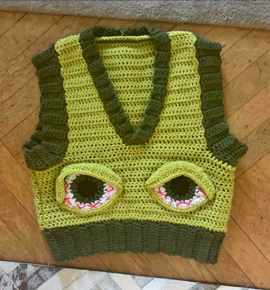 A green crochet vest with large, stylized eyes on the front, an unconventional craft project.