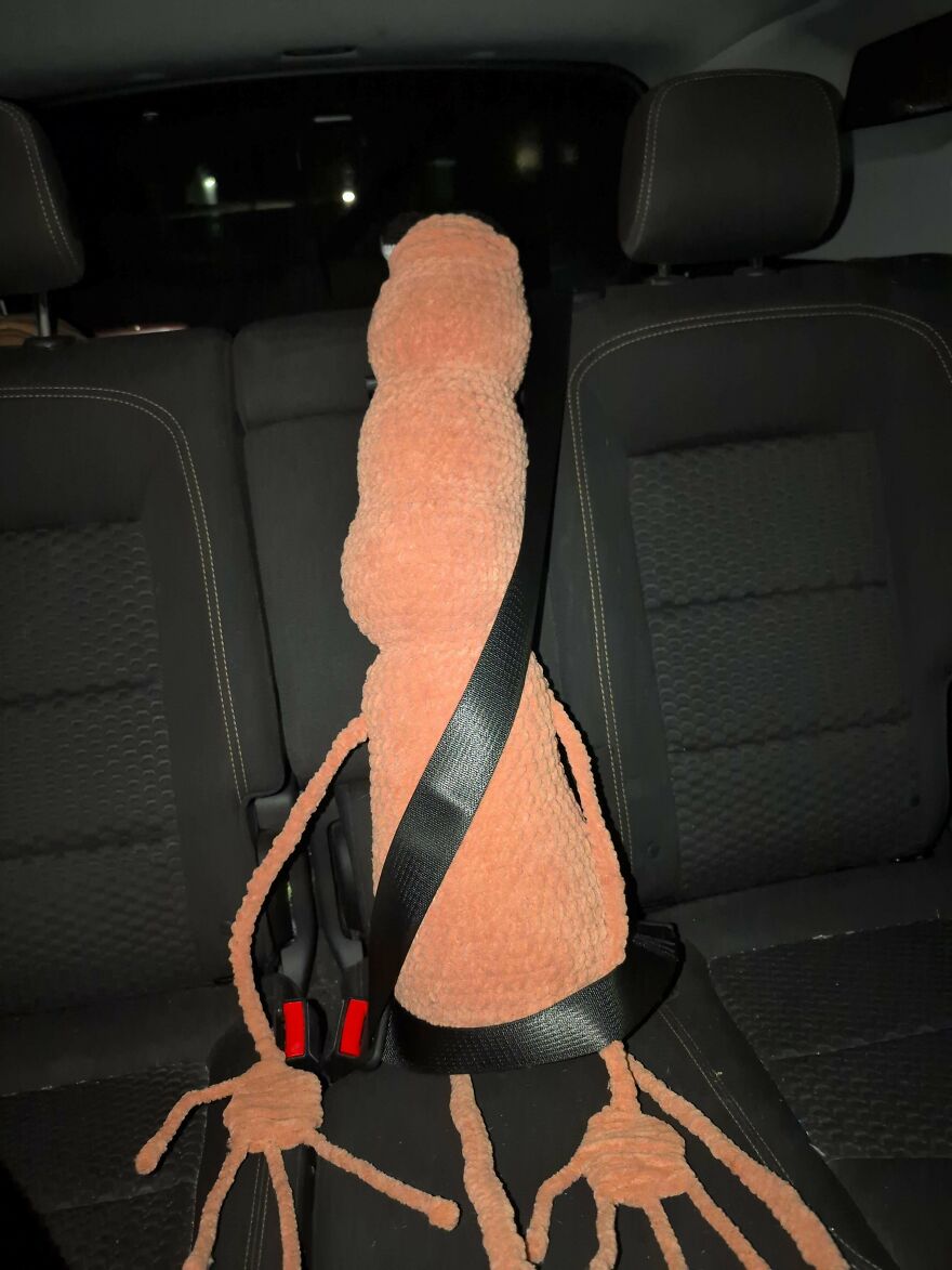 A long, peach-colored crochet creation buckled into a car seat, a quirky craft project.