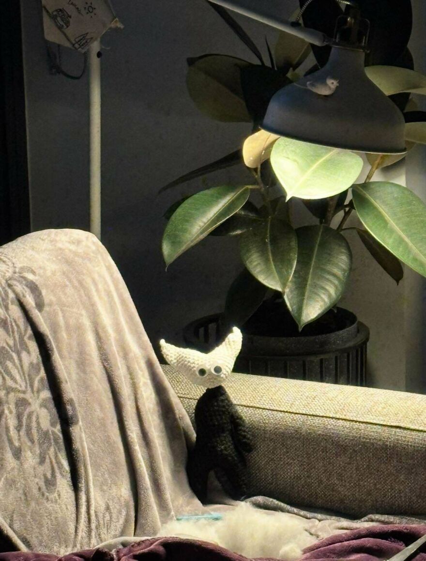 A small, white and black crochet creation sitting on a sofa, a cozy craft project under a lamp.