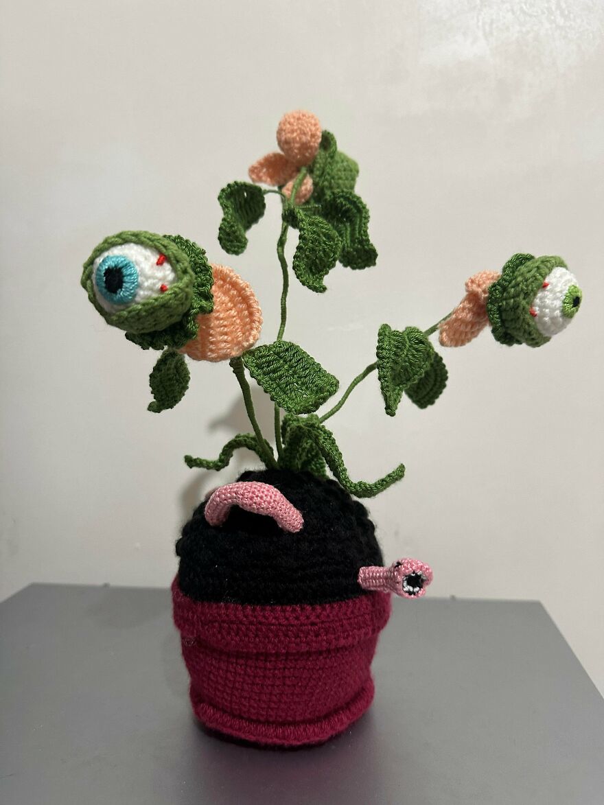 A peculiar crochet creation: a potted plant with eyeballs and worms, proving craft projects turn out uniquely.