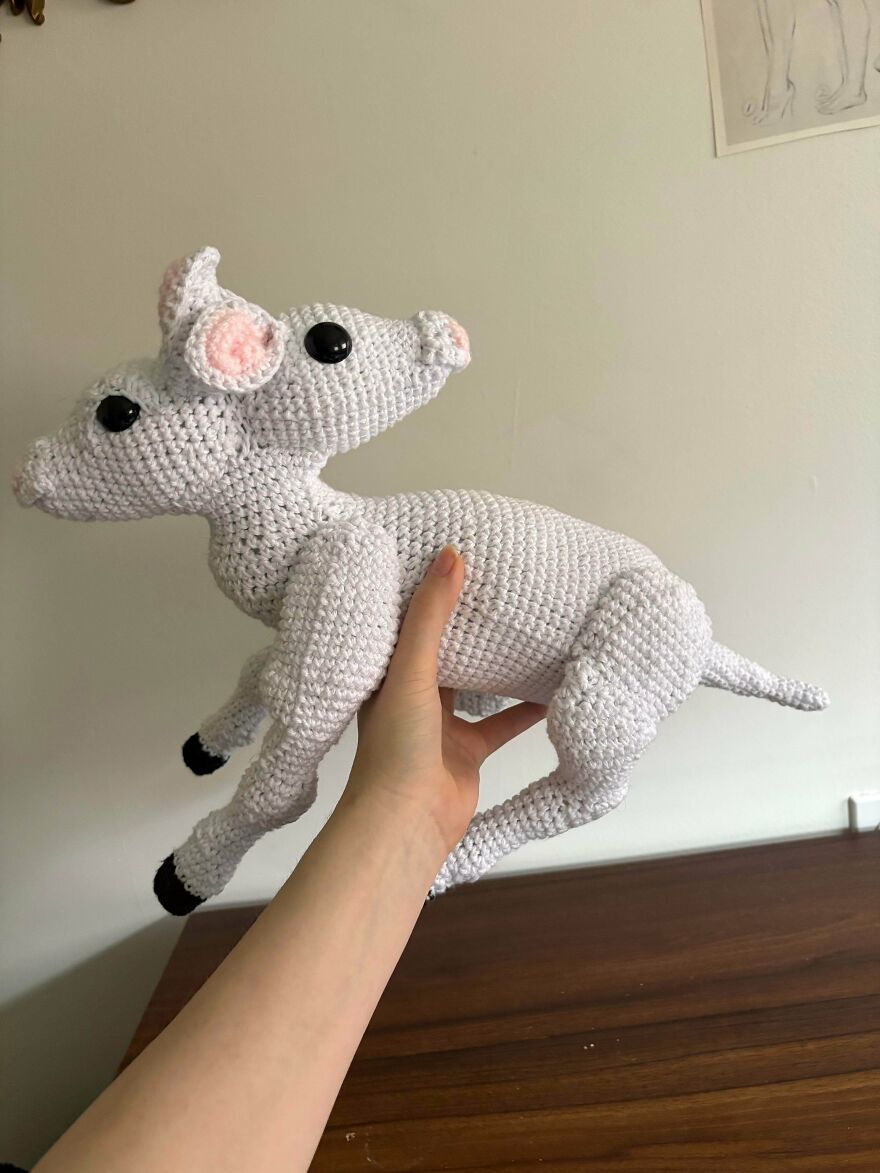 A hand holds a white crochet deer with pink ears and black hooves, a unique craft project.