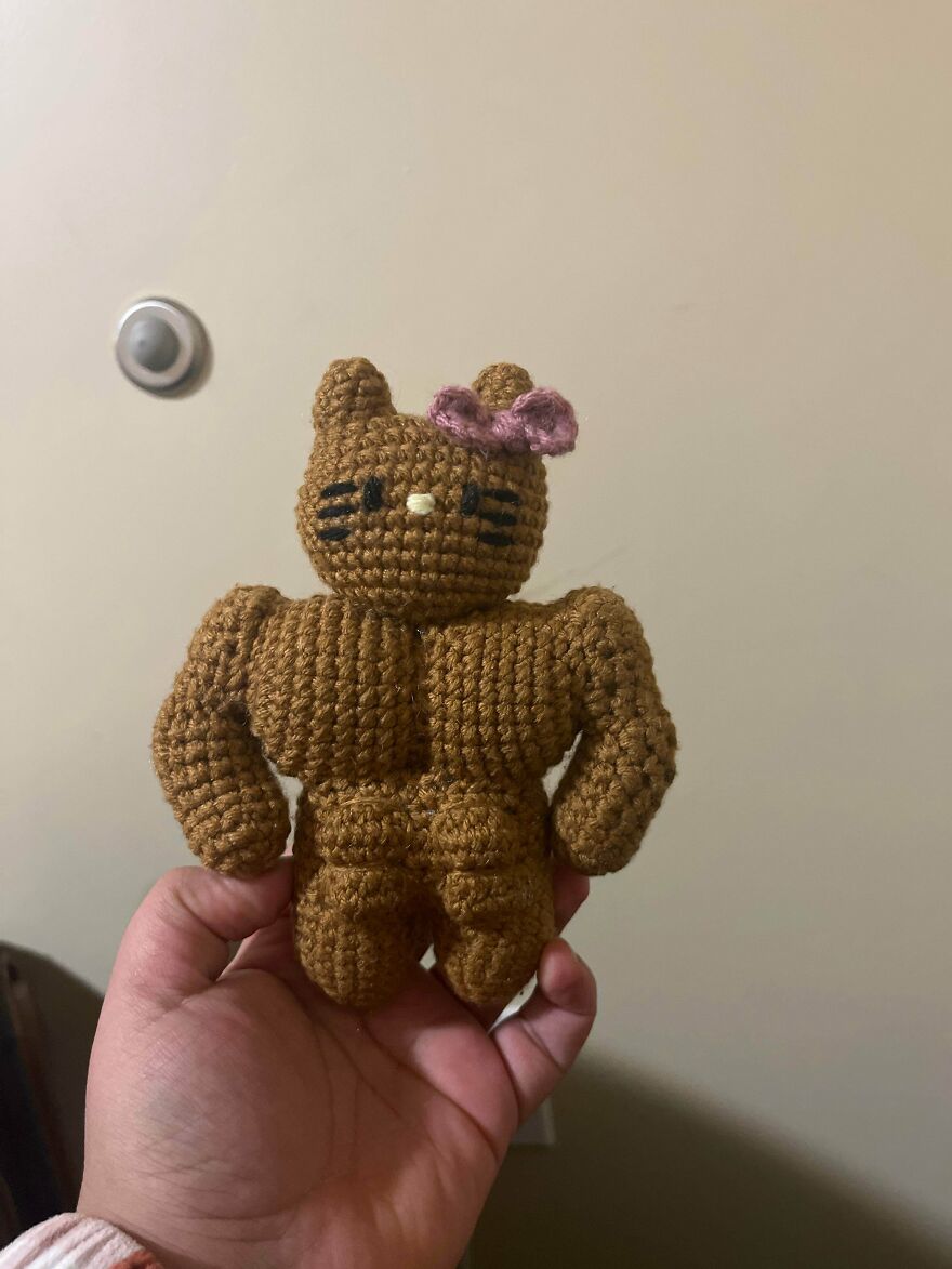 A hand holds a muscular crochet Hello Kitty, a humorous craft project not as intended.
