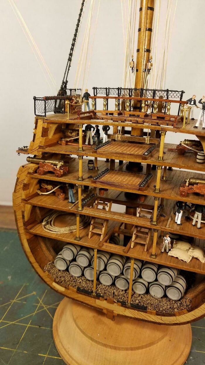 A detailed cross-section of a wooden ship model, showing multiple decks with tiny figures, cannons, and barrels, an interesting object cut in half.