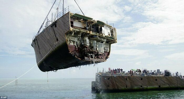 An interesting photo of an object cut in half: a large ship hull being lifted by cranes, exposing its internal structure.