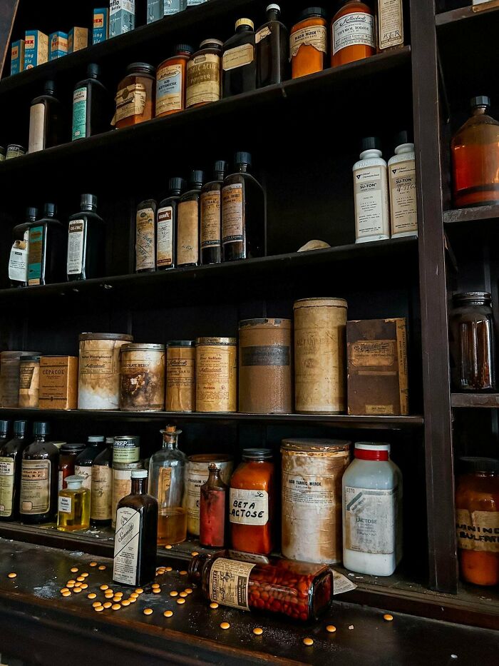 Exploring abandoned places shows a shelf filled with antique apothecary jars, bottles, and scattered pills.