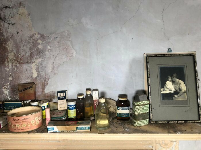 Exploring abandoned places unveils old medicine bottles, beauty products, and a framed photograph on a dusty mantelpiece.