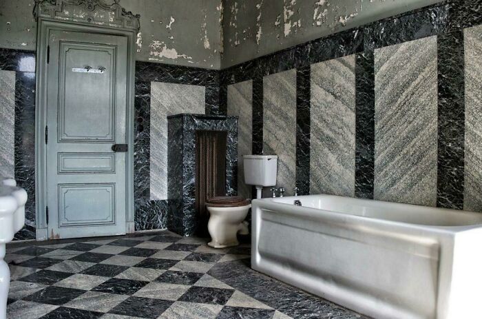 Exploring abandoned places: an elegant but decaying bathroom with marble walls, a bathtub, and a checkerboard floor.