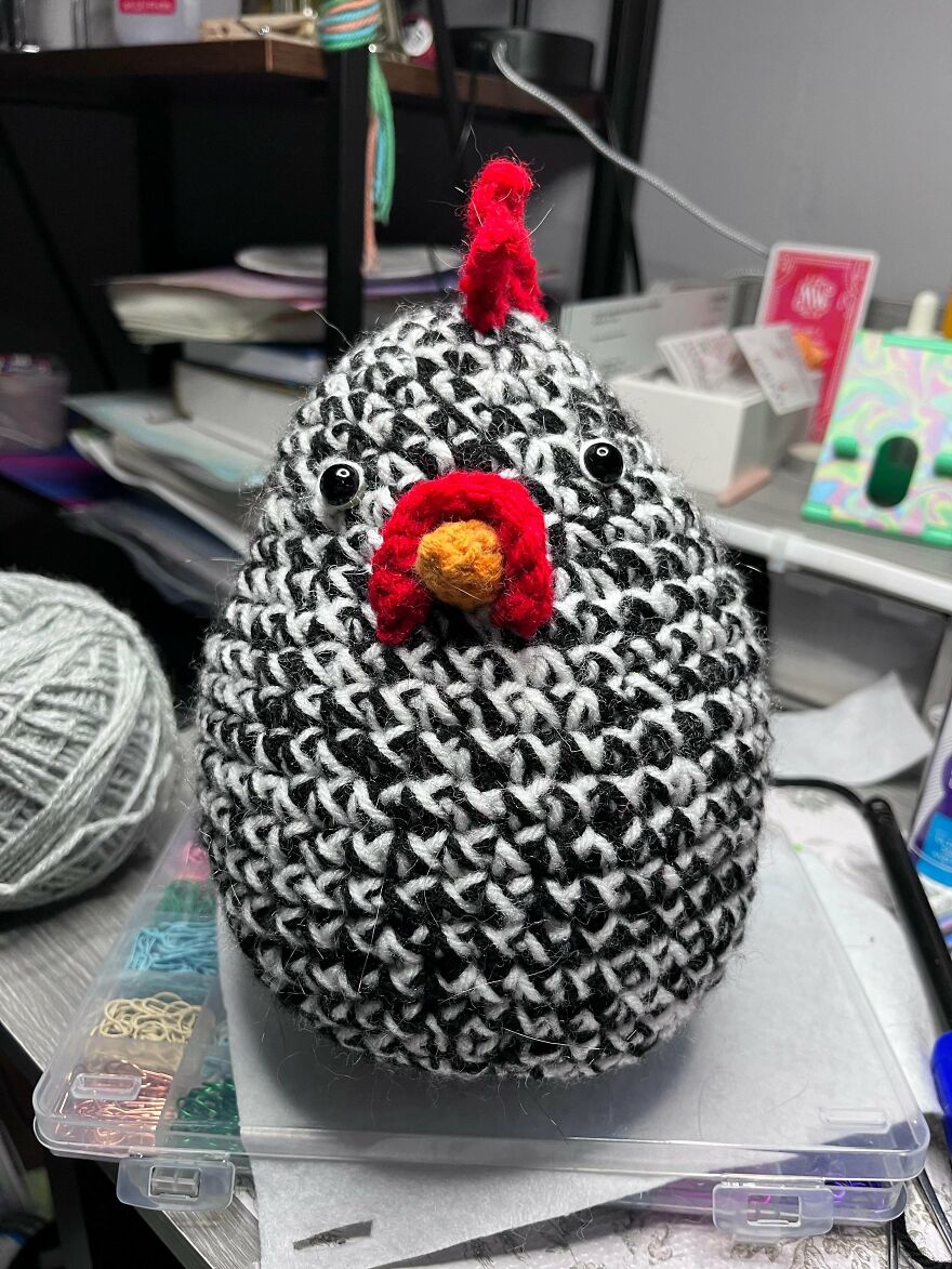 A black and white speckled crochet creation chicken with a red comb, showcasing a fun craft project.