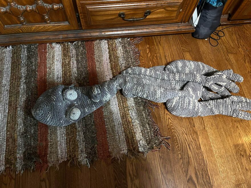 A long, grey, alien-like crochet creation lies on a striped rug. Crochet craft projects.