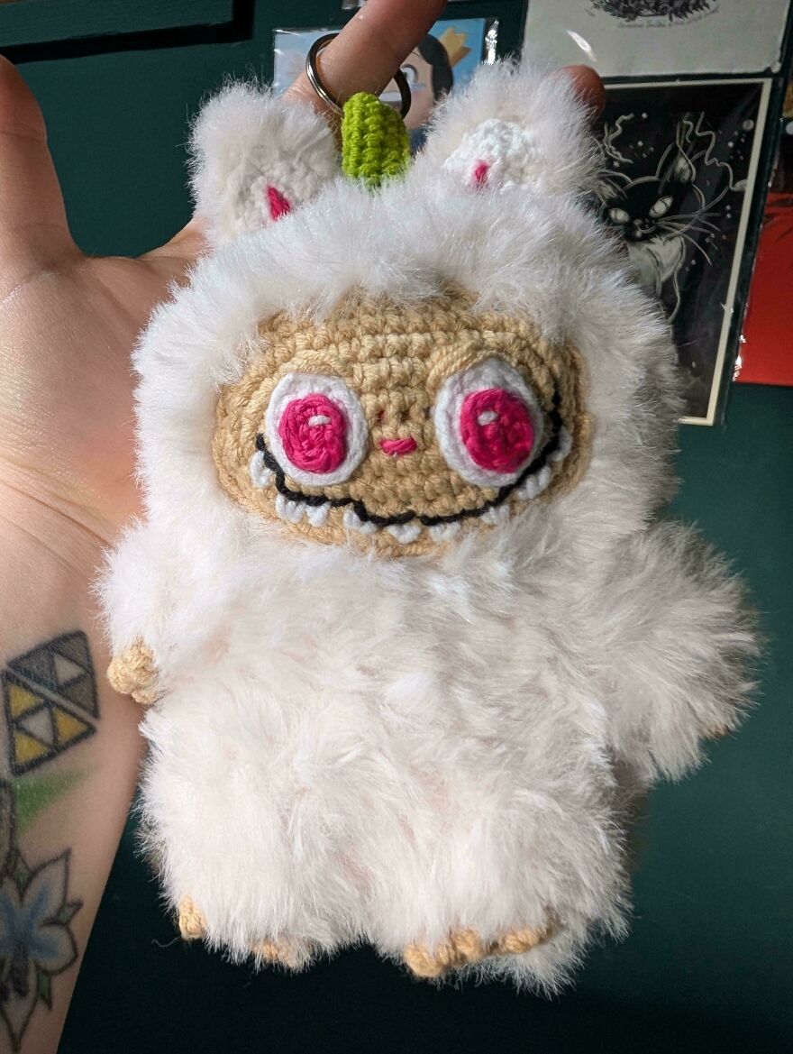 A fluffy white crochet creation with pink eyes and a wide smile, held in a hand. Crochet craft projects.