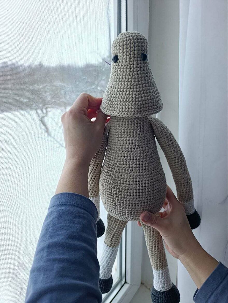 A tall, beige crochet creation with black eyes held up by hands, an example of crochet crafts.
